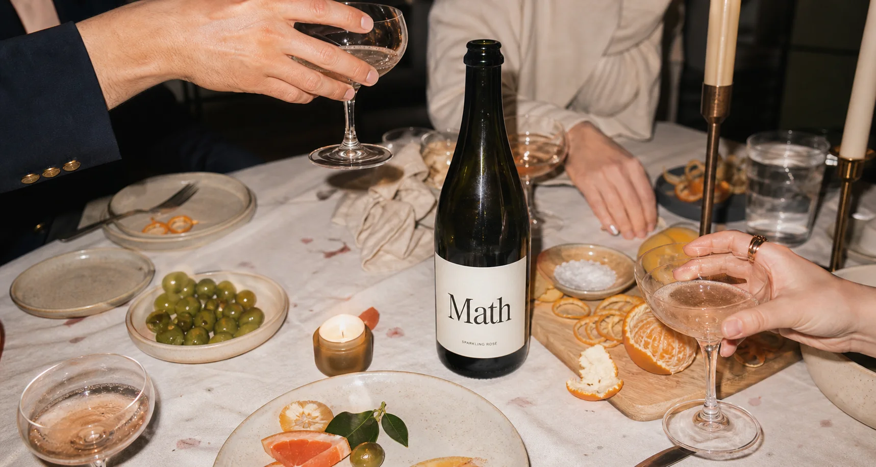 Math Wine bottle on a dinner-party table with coupe glasses, citrus and candles